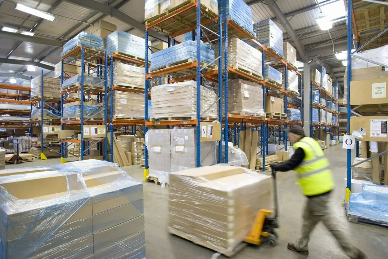 A man pushing a cart in a warehouse filled with boxes.